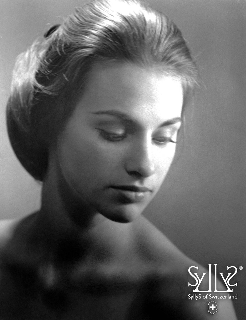 An elegant black and white image of founder Syllys of Switzerland back in her 20s. She is looking down over her shoulder with a classic movie star large bun style sitting right above her shoulders mid neck.
